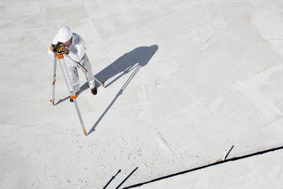 Surveyor in white protective gear using a theodolite on a concrete surface.