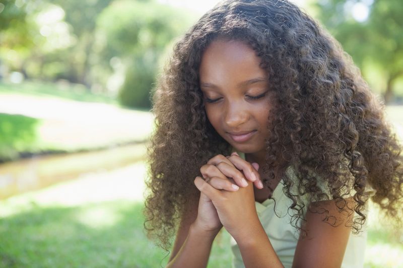 Young girl praying in the park on a sunny day