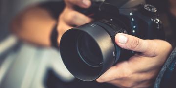 Close-up of hands holding a DSLR camera with a large lens.