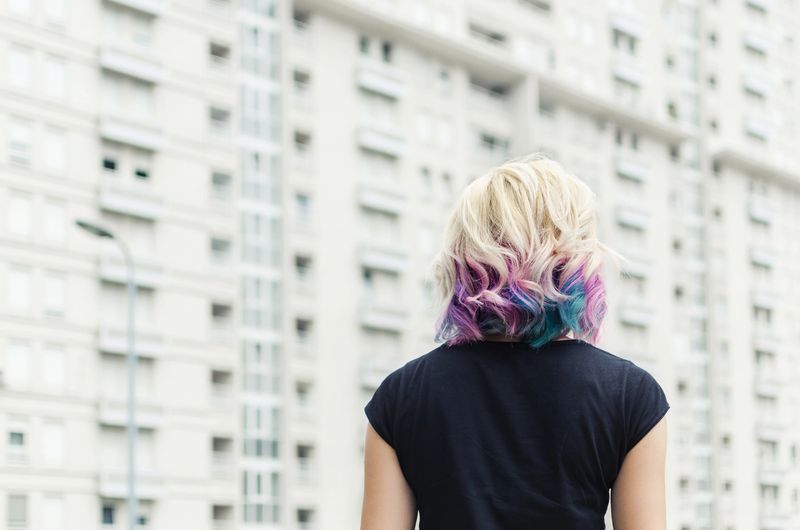 Beautiful female with rainbow or unicorn hair watching big buildings in the city outdoors or outside. Back view.