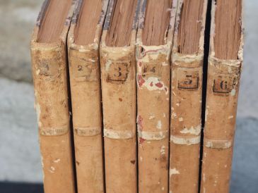 A row of six old, worn books with numbered spines.