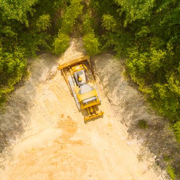 A bulldozer clearing a path through a forested area from above.