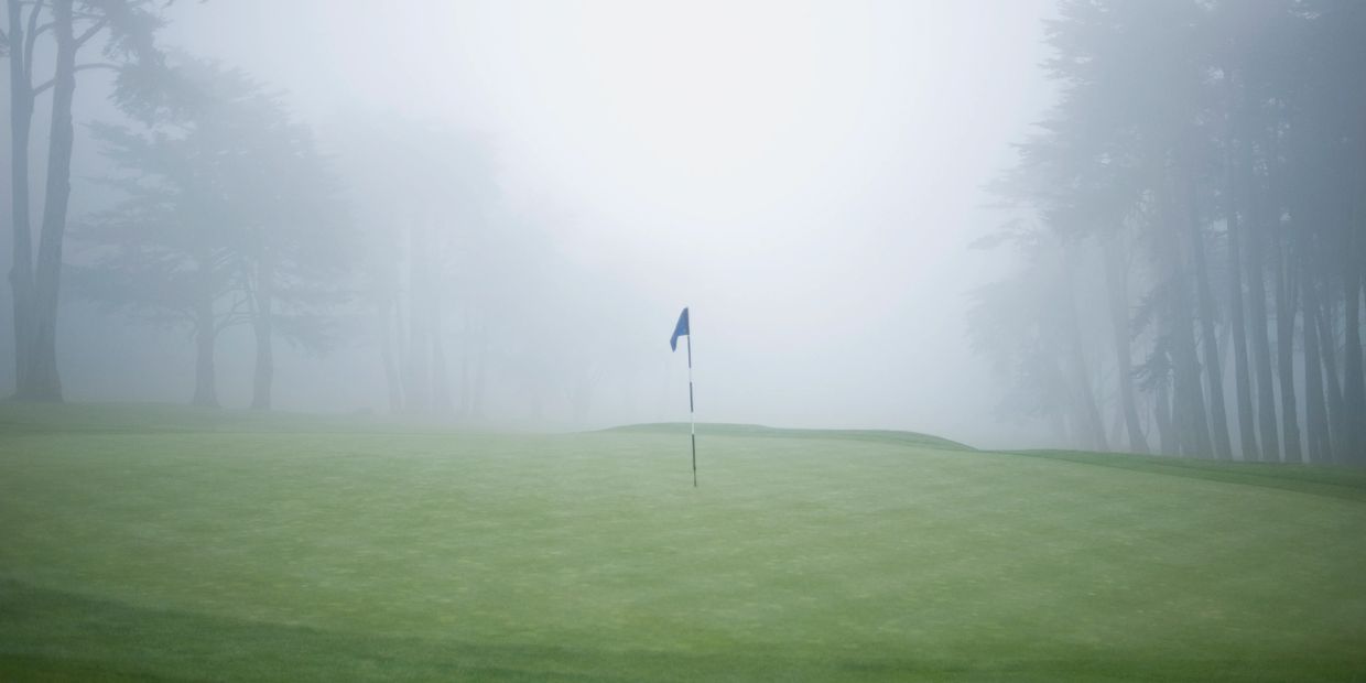 Foggy golf course with flag on the green surrounded by trees.