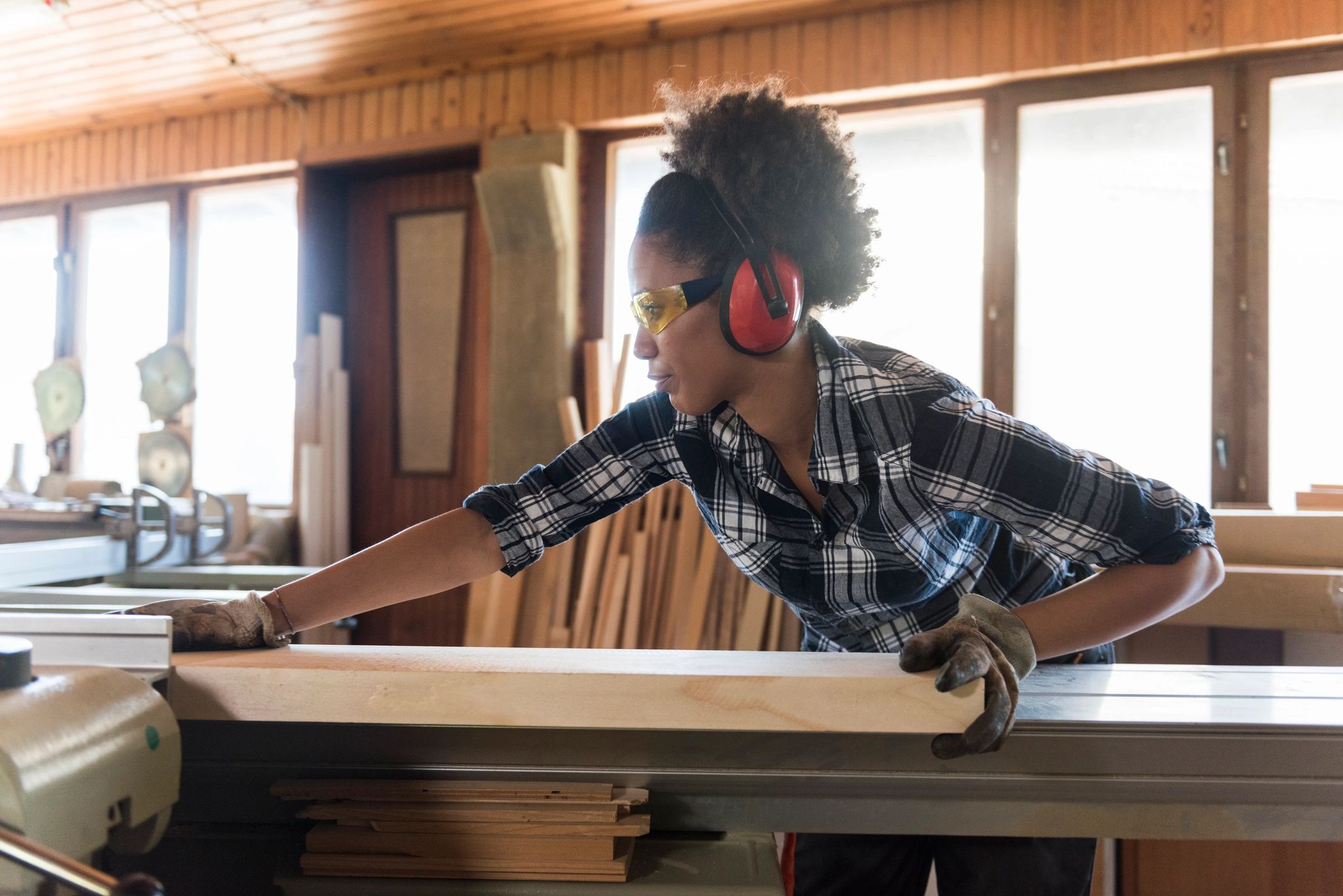 Woman using woodworking machine in a workshop with safety gear.