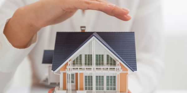 Hand protecting a small house model.