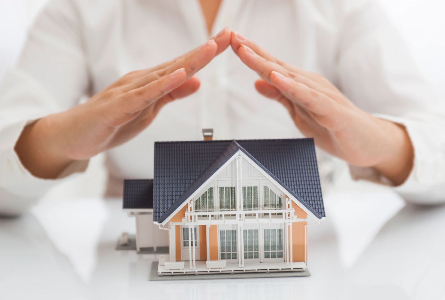 Hands protecting a miniature house model symbolizing home protection.