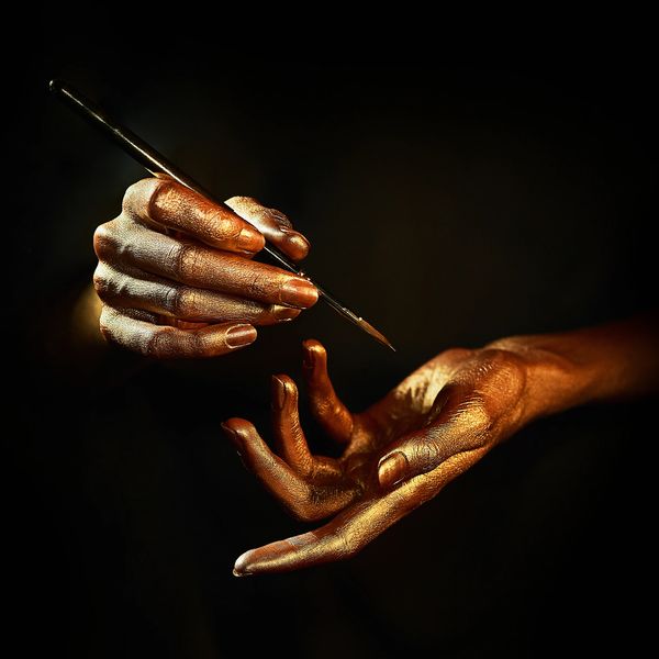 Golden-painted hands with a brush painting details on a finger.