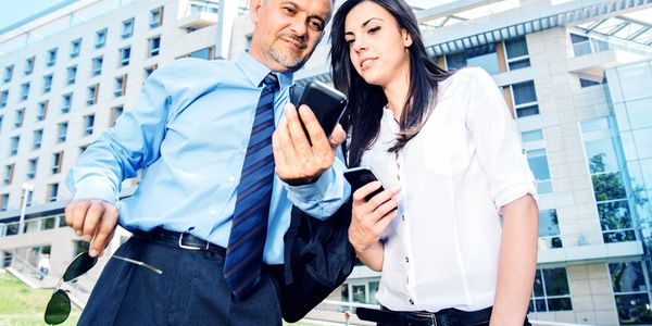 Two professionals looking at a smartphone outside an office building.