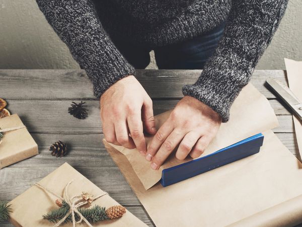 Person wrapping a gift with brown paper and blue tape dispenser.