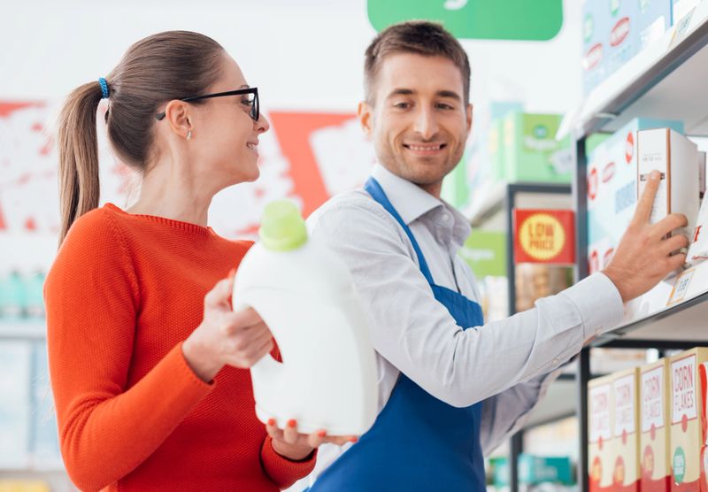 Professional supermarket clerk helping a customer, she is showing him a laundry detergent product