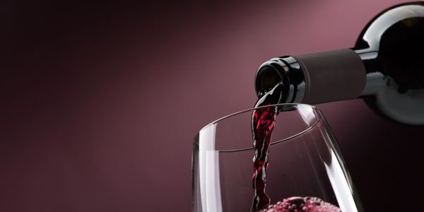 Red wine being poured into a tilted glass against a soft maroon background.