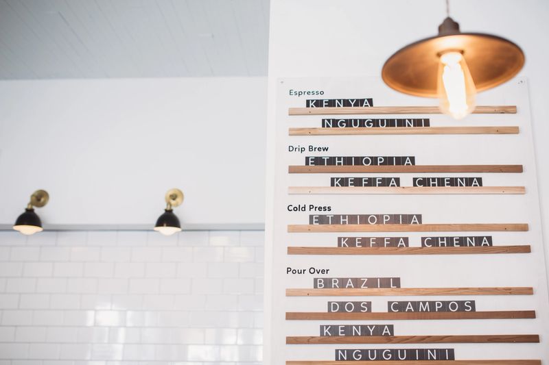 A clean and bright cafe menu board, offering fresh single origin espresso drinks and coffee beans from a variety of countries and locations.