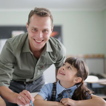 Teacher smiling at a young girl in a classroom.