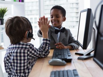 Two young boys high-fiving in front of computer screens during a fun activity.