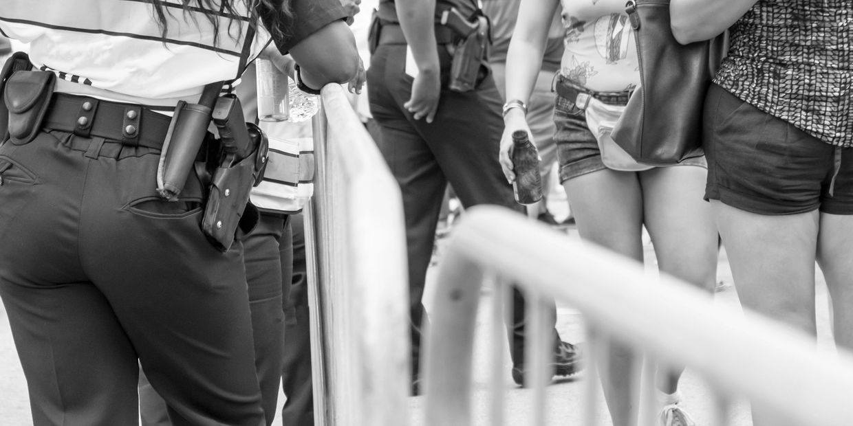 Police officers in reflective vests stand behind barricades near casually dressed people.