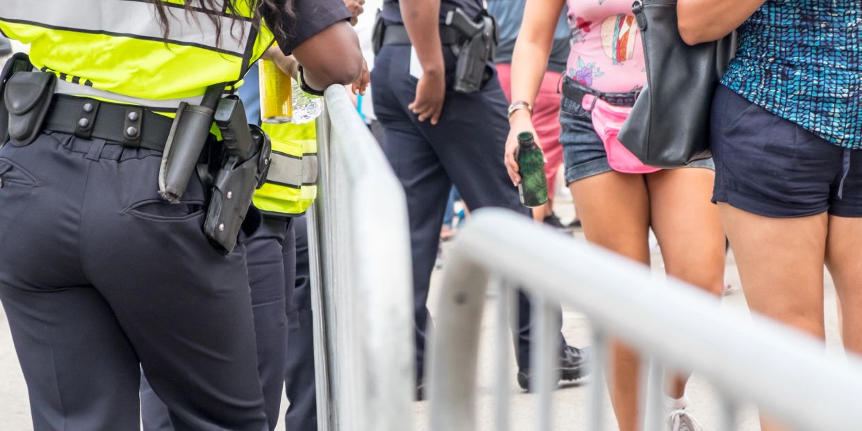 Police officers in reflective vests stand behind barricades near casually dressed people.