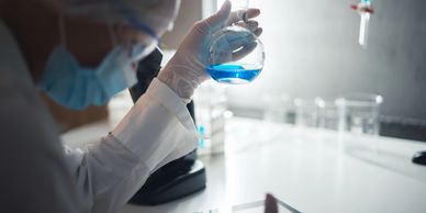 Scientist examining blue liquid in a laboratory flask.