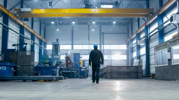 A worker walks in a spacious, modern industrial facility wearing a blue hard hat.