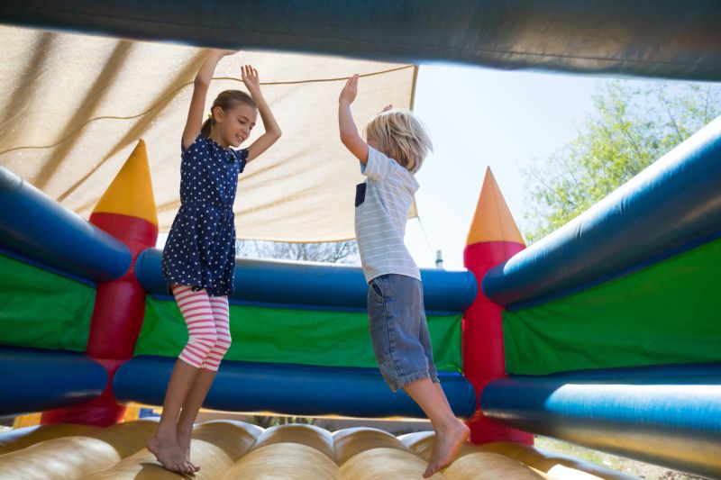 Happy siblings with arms raised jumping on bouncy castle at playground