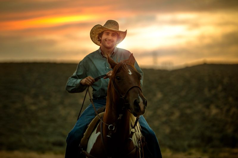 A handsome young cowboy rides on his horse at sunset.