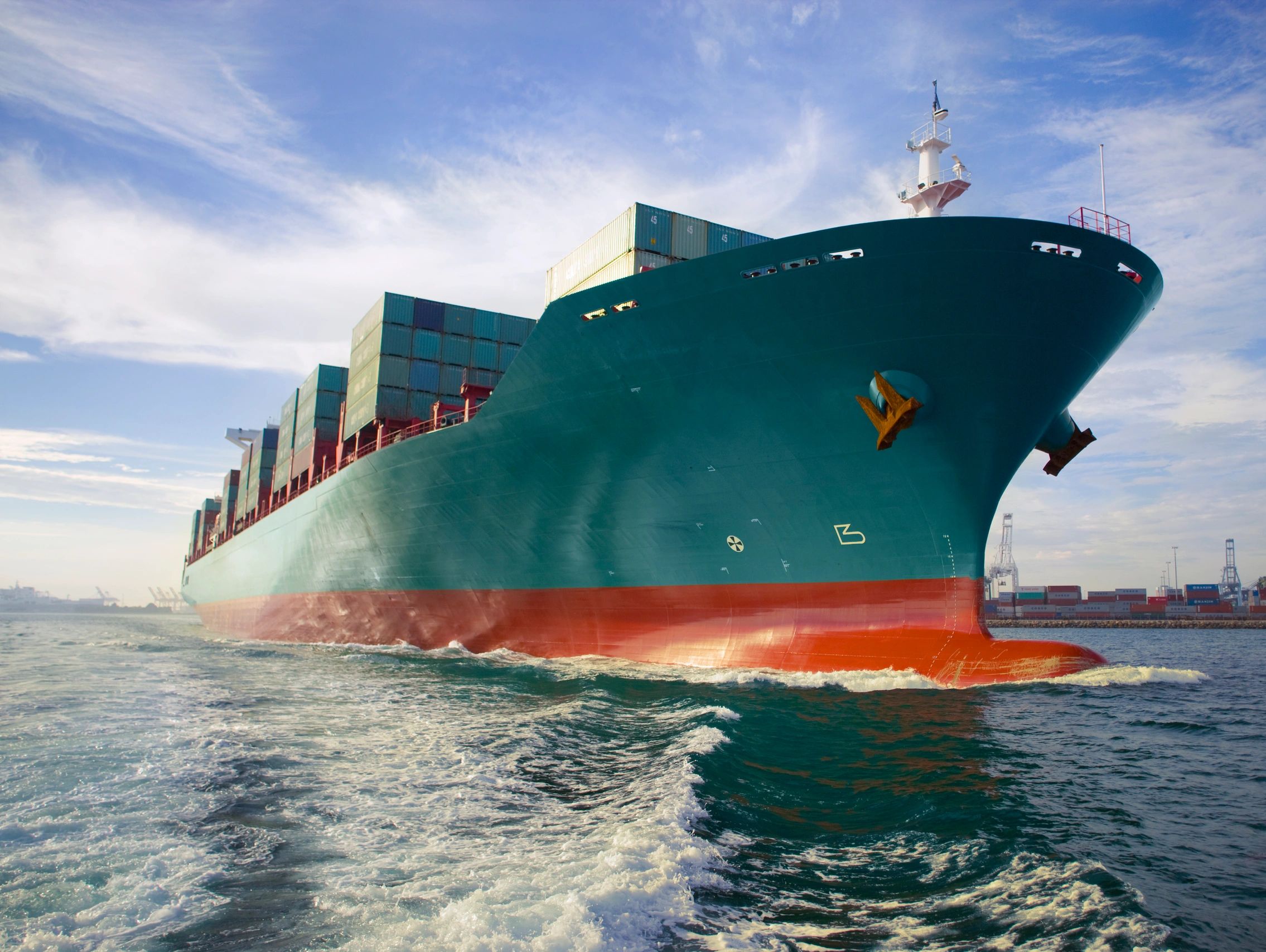 Large container ship sailing near port cranes.