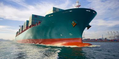 Large cargo ship loaded with containers sailing near a port under blue sky.