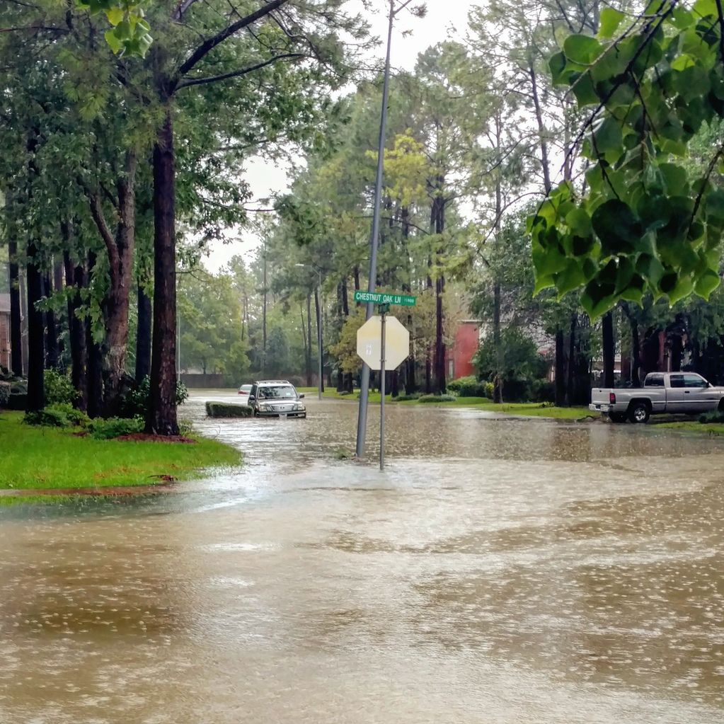 A residential street flooded with rainwater, partially submerging cars and traffic signs.