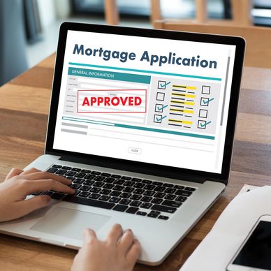 Person viewing an approved mortgage application on a laptop with a smoothie and phone nearby.