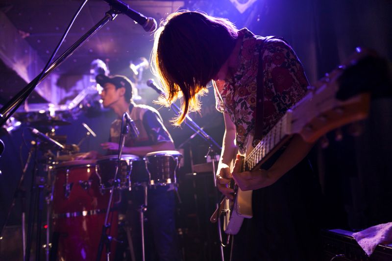 A young Japanese woman is playing the guitar during a live band event.