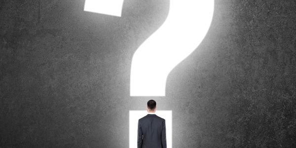 Man in suit facing a giant illuminated question mark on a dark wall.