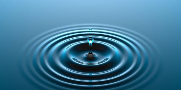 Close-up of a water droplet creating ripples on a calm surface.