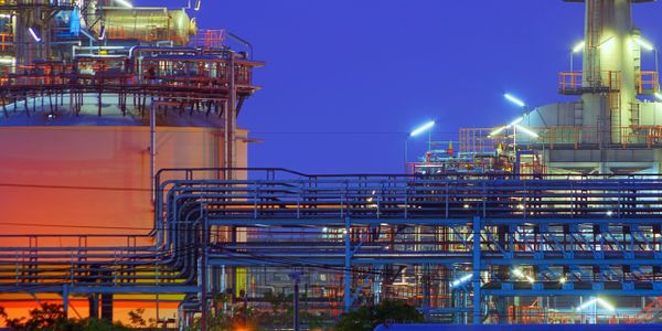 Industrial refinery with extensive piping and storage tanks at dusk.