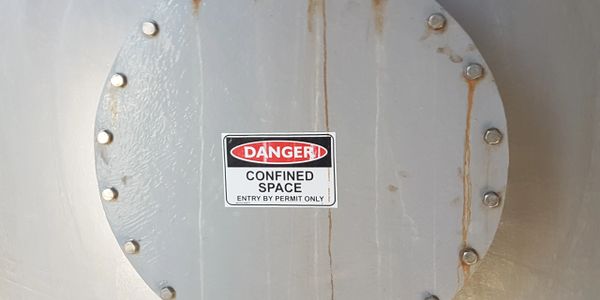 Metal hatch with a danger sign indicating a confined space requiring a permit to enter.