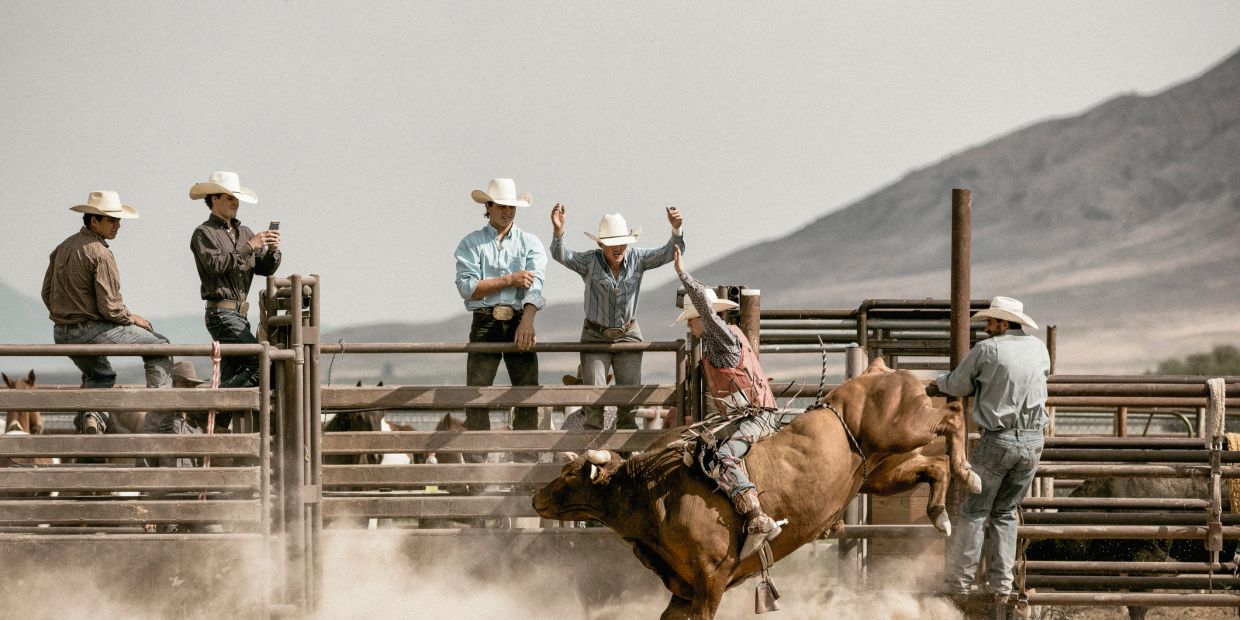 Cowboy riding a bucking bull in a rodeo arena with spectators watching.