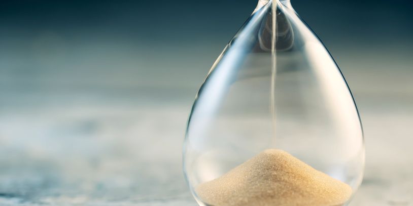 Close-up of sand flowing through an hourglass on a wooden surface.