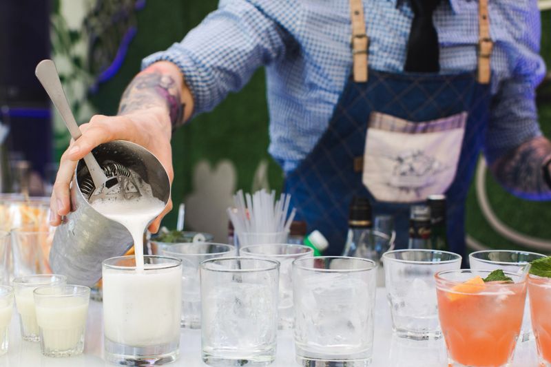 Faceless person holding metal shaker and pouring freshly made cocktails in glasses on banquet.