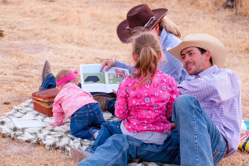 Young Western Family having a picnic on a plaid blanket on the Ranch and reading a book together.
