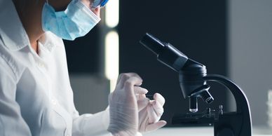 Scientist in protective gear prepares a sample near a microscope in a lab.