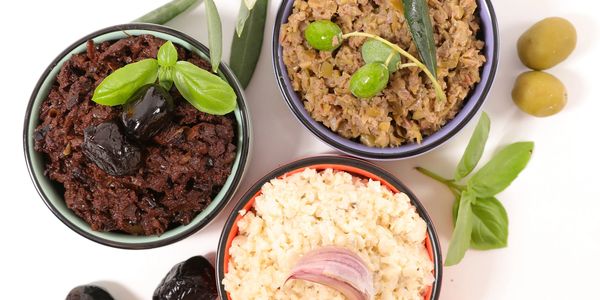 Three bowls of different olive tapenades with fresh herbs and olives.