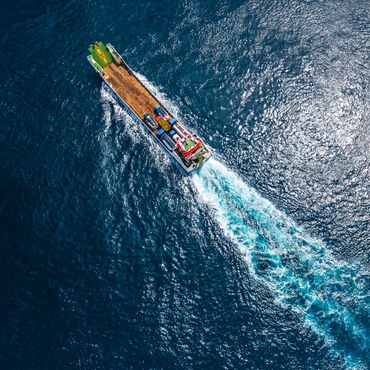 Aerial view of a cargo ship moving through deep blue ocean water.