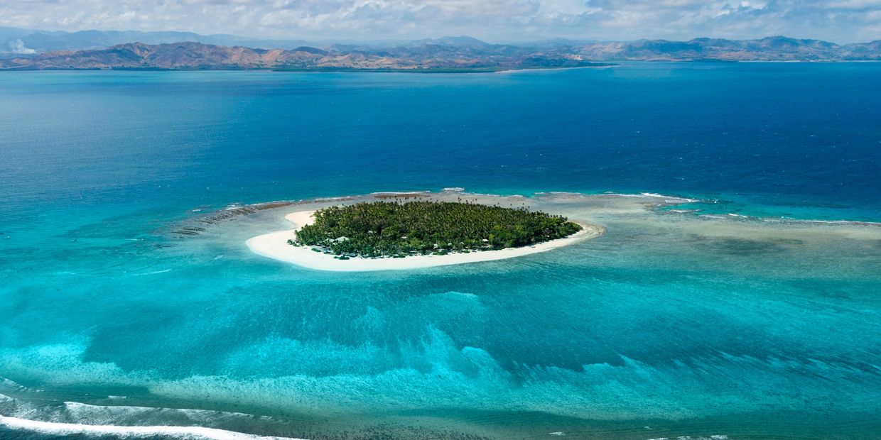 A small tropical island surrounded by clear blue waters and coral reefs.