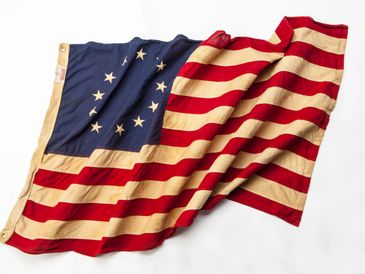 Worn Betsy Ross American flag with 13 stars in a circle and red and white stripes.