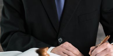 A person in a suit signing a document with a gavel nearby.