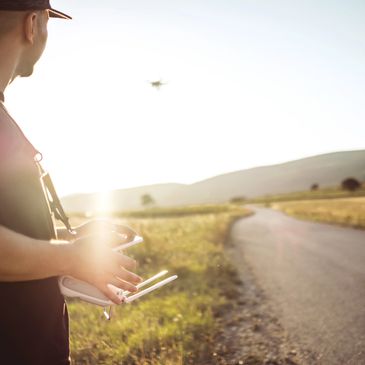 Man operating a drone controller outdoors near a winding road at sunset.
