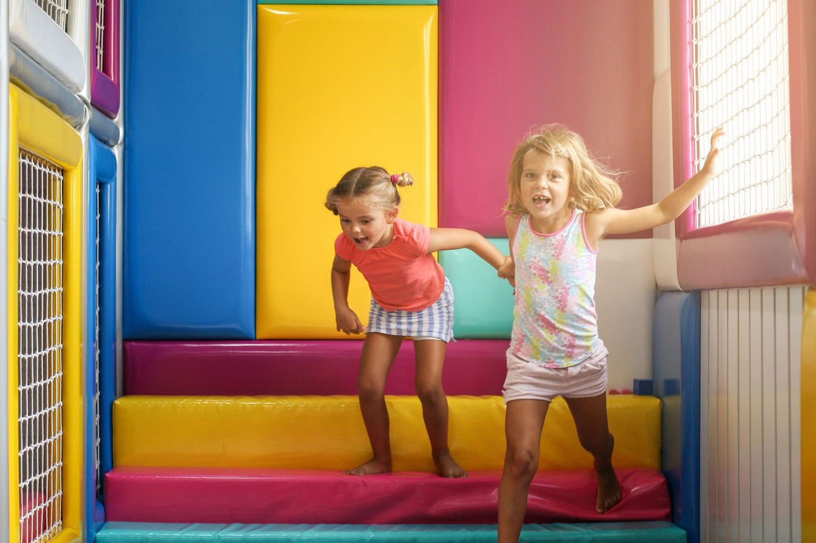Two girls playing energetically in a colorful soft play area.