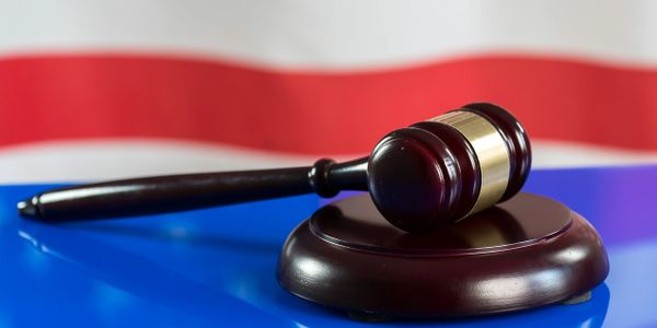 A judge's gavel on a reflective surface with an American flag backdrop.