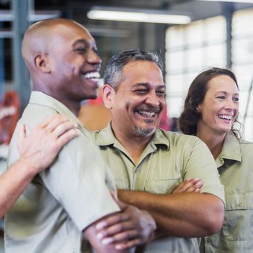 Three diverse workers smiling and standing together in a workplace.