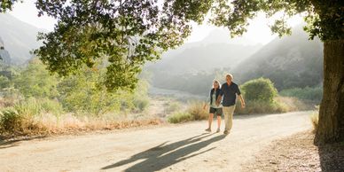 older couple walking on path surrounded by trees