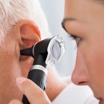 Doctor examining elderly man's ear with otoscope.