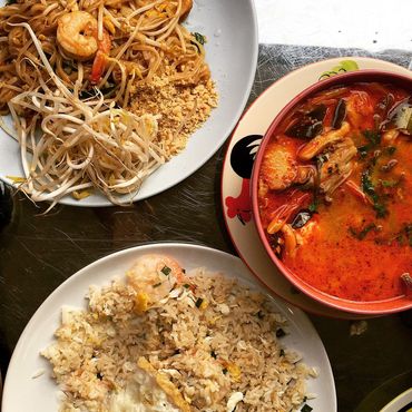 A spread of Thai dishes including pad thai, fried rice, and tom yum soup with rice and condiments.